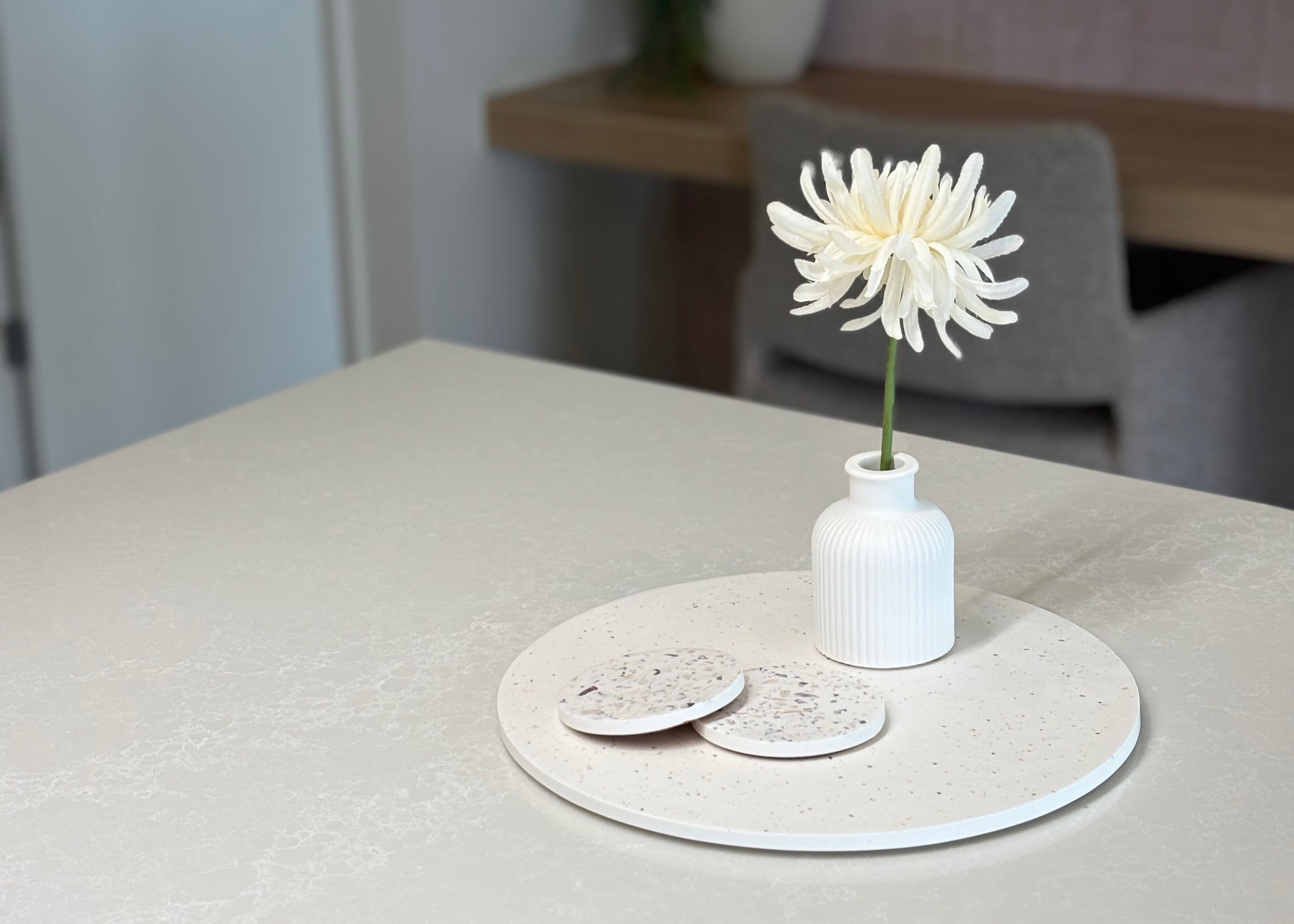 White round platter on a kitchen counter styled with seashell terrazzo coasters and a single flower in a bud vase.