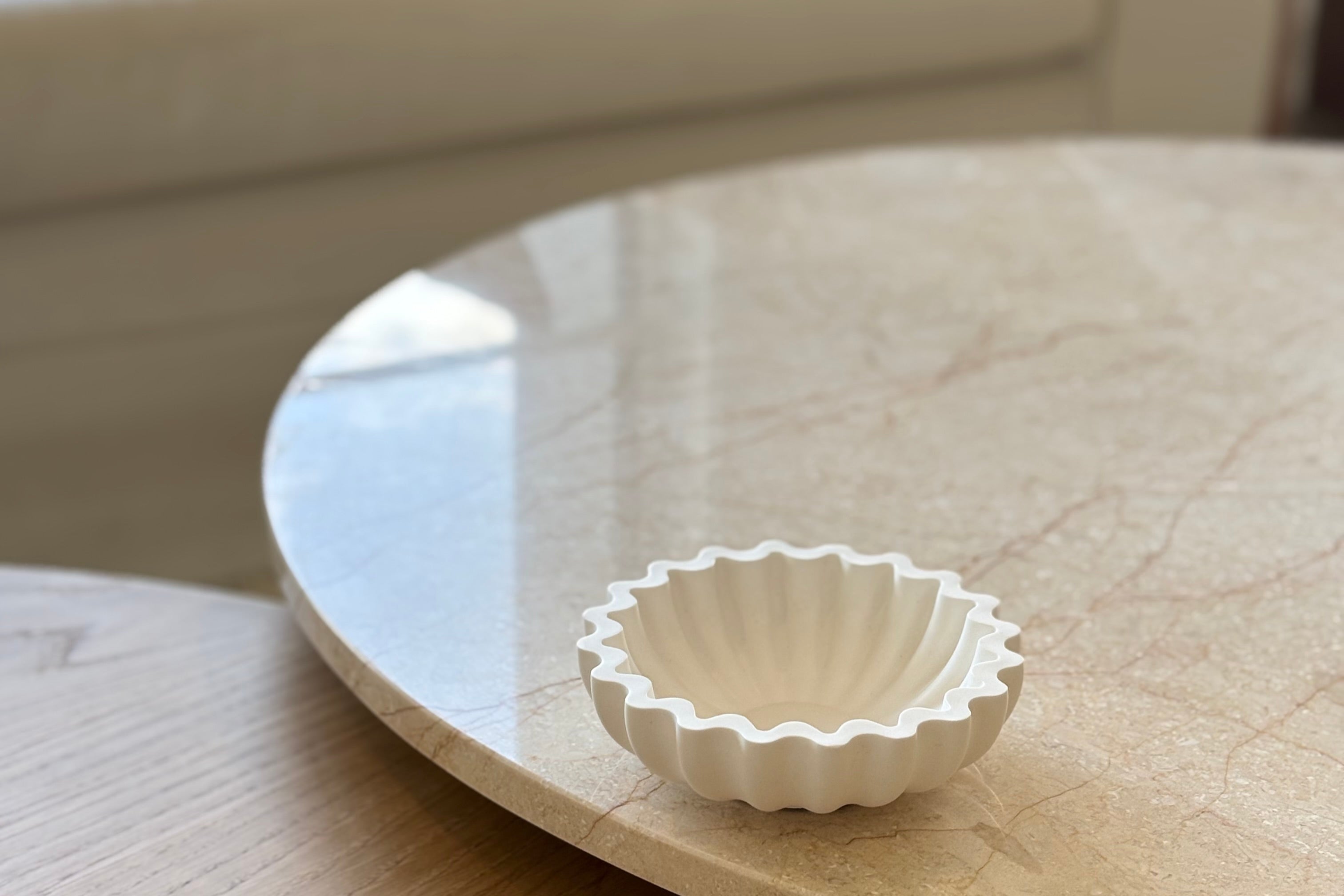 Small white decorative bowl on a round marble coffee table with a blurred sofa in the background.